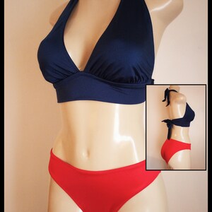 May include: Navy blue halter bikini top and red bikini bottoms. The top has a V-neck design and ties at the neck and back. The bottoms are a classic brief style. The swimsuit is displayed on a mannequin.