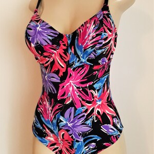 May include: A black swimsuit with a floral print in shades of pink, purple, and blue. The swimsuit has a V-neckline and adjustable straps.