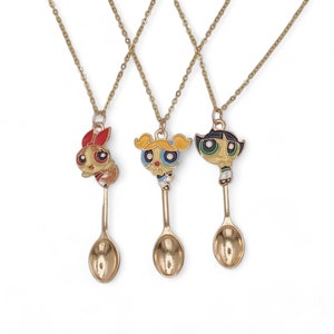 May include: Three gold-colored necklaces featuring cartoon character pendants attached to spoon-shaped charms. The pendants depict characters with red, yellow, and black accents. The necklaces are displayed against a white background.