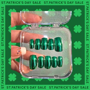 May include: A clear plastic container with a hinged lid holds a set of ten green metallic press-on nails. The nails are arranged in two rows of five, with the tips facing up.