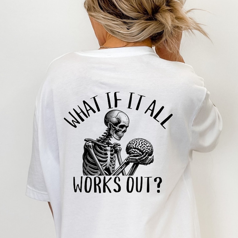 Op de afbeelding: Wit T-shirt met een zwart-witte afbeelding van een skelet dat een hersenen vasthoudt. De tekst "What if it all works out?" staat op het shirt gedrukt.