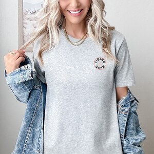 Op de afbeelding: Een grijs T-shirt met een zwarte cirkelvormige afbeelding met de tekst "Vibing Mind" in wit.