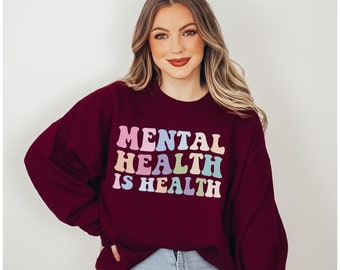 Op de afbeelding: Bordeauxkleurig sweatshirt met de tekst "MENTAL HEALTH IS HEALTH" in regenboogkleuren.
