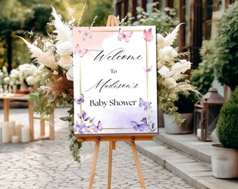 May include: Welcome to Madison's Baby Shower sign with a watercolor background featuring purple butterflies and flowers. The sign is on a wooden easel.