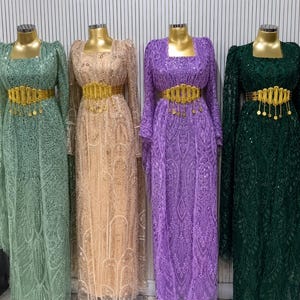 Könnte beinhalten: Vier langärmelige, bodenlange Kleider in Hellgrün, Beige, Lila und Dunkelgrün. Jedes Kleid verfügt über ein kompliziertes Paillettenmuster, einen eckigen Ausschnitt und einen breiten goldfarbenen Metallgürtel mit hängenden runden Akzenten.