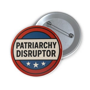 May include: A circular badge with the words "PATRIARCHY DISRUPTOR" in black. The design features a red and blue border with three white stars. A second, silver-coloured badge is visible in the background.