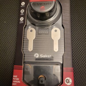 May include: A black and red picture hanging and leveling tool with a clear plastic cover. The tool has a level, a measuring tape, and a hook. The packaging says "Saker" and "Make picture hanging easy!"