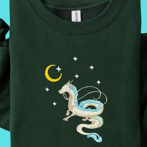 Op de afbeelding: Donkergroene sweatshirt met een borduursel van een witte en blauwe draak, een gele halve maan en witte sterren. De top met lange mouwen heeft een ronde hals en omgeslagen manchetten.