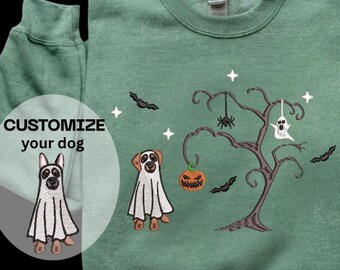 Puede incluir: Sudadera verde con un diseño temático de Halloween. El diseño incluye un árbol con arañas colgantes, una calabaza y un fantasma. La sudadera también presenta dos perros disfrazados de fantasmas. El texto a la izquierda dice "CUSTOMIZE your dog".