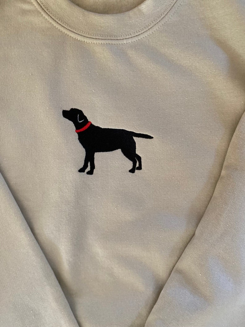 May include: A light gray sweatshirt with a black embroidered silhouette of a Labrador Retriever wearing a red collar.