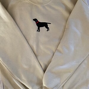 May include: A beige sweatshirt with a black embroidered Labrador Retriever wearing a red collar.