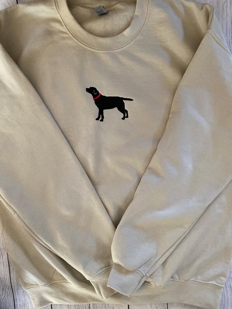 May include: A beige sweatshirt with a black embroidered Labrador Retriever wearing a red collar.