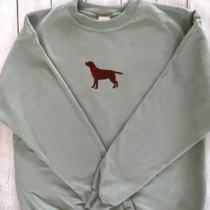 May include: A sage green sweatshirt with an embroidered brown Labrador Retriever wearing a red collar.