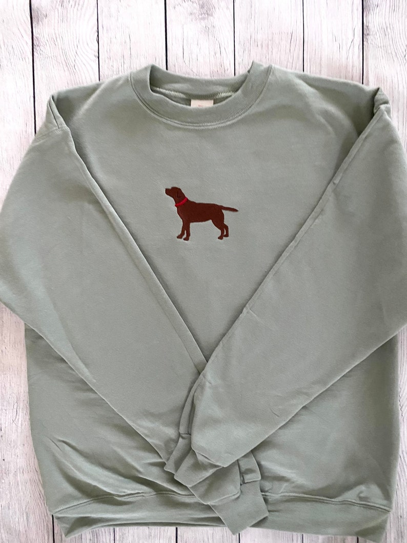 May include: A sage green sweatshirt with an embroidered brown Labrador Retriever wearing a red collar.