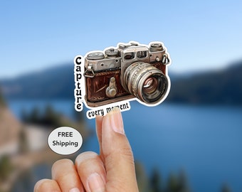May include: A vintage camera sticker with a brown leather body and a silver lens. The sticker has the text "Capture every moment" printed on it.