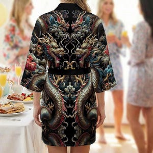 Op de afbeelding: Zwarte kimono-achtige badjas met een drakenontwerp. De badjas heeft een gedetailleerde illustratie van draken in goud, rood en blauw op een zwarte achtergrond. Het heeft een zwarte riem en korte mouwen. De afbeelding toont de achterkant van de badjas.