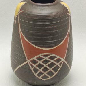 Könnte beinhalten: Eine braune Keramikvase mit einem geometrischen Muster in Weiß, Gelb und Orange. Die Vase hat eine strukturierte Oberfläche und eine abgerundete Form.