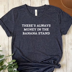 May include: A dark heather grey t-shirt with the text "There's always money in the banana stand" printed in white.