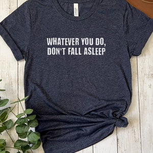May include: A dark heather grey t-shirt with the text "Whatever you do, don't fall asleep" printed in white.