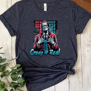 May include: A dark heather grey t-shirt with a graphic of a monster in a suit with the text "Creep it Real".