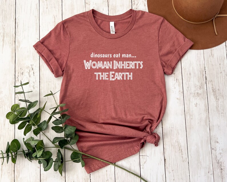 Peut inclure: Un t-shirt marron avec le texte "dinosaurs eat man... WOMAN INHERITS THE EARTH" en blanc.