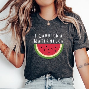 Może przedstawiać: Szary t-shirt z napisem "I carried a watermelon" i grafiką czerwonego plastra arbuza z czarnymi pestkami i zieloną sk&oacute;rką.