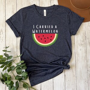 Może przedstawiać: Koszulka w ciemnoniebieskim kolorze z napisem "I carried a watermelon" i grafiką plasterka arbuza z czerwonym miąższem i czarnymi pestkami.