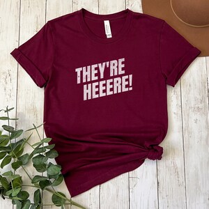 K&ouml;nnte beinhalten: Ein maroonfarbenes T-Shirt mit dem Aufdruck "They're Heeeeere!" in wei&szlig;.