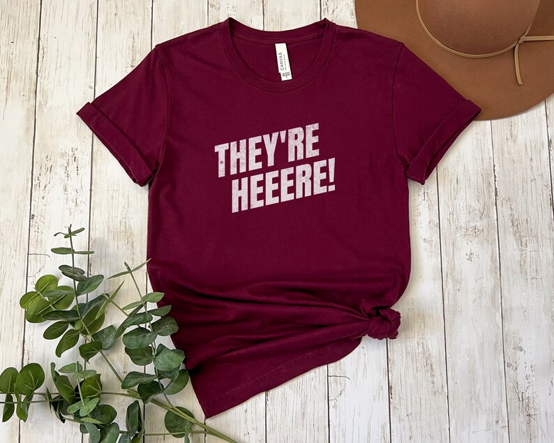 K&ouml;nnte beinhalten: Ein maroonfarbenes T-Shirt mit dem Aufdruck "They're Heeeeere!" in wei&szlig;.