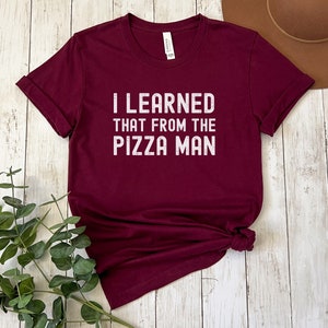 May include: A maroon t-shirt with the text "I learned that from the pizza man" printed in white.