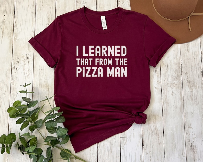 May include: A maroon t-shirt with the text "I learned that from the pizza man" printed in white.