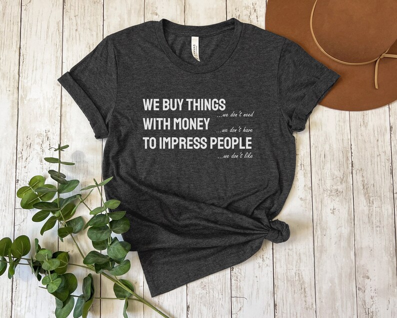 Może przedstawiać: Szary t-shirt z nadrukiem "WE BUY THINGS...we don't need WITH MONEY...we don't have TO IMPRESS PEOPLE...we don't like" w kolorze białym.