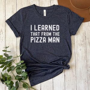 May include: A dark heather gray t-shirt with the text "I LEARNED THAT FROM THE PIZZA MAN" printed in white.