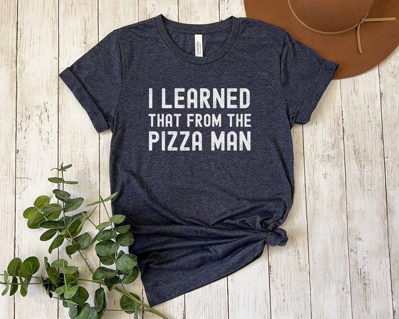 May include: A dark heather gray t-shirt with the text "I LEARNED THAT FROM THE PIZZA MAN" printed in white.