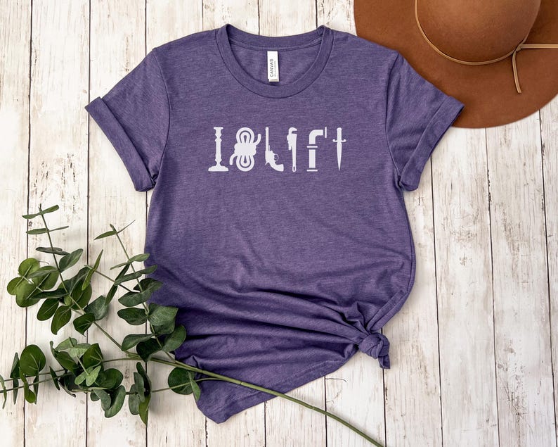 May include: Purple short-sleeved t-shirt with the text "I  LIFT" in white lettering. The text is made up of various tools, including a wrench, a hammer, a screwdriver, and a knife.