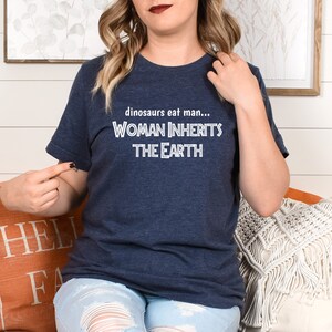 Peut inclure: Un t-shirt bleu marine avec un texte blanc qui dit "dinosaurs eat man... WOMAN INHERITS THE EARTH"