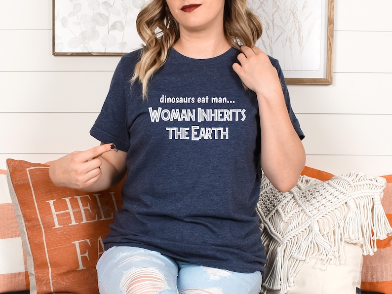 Peut inclure: Un t-shirt bleu marine avec un texte blanc qui dit "dinosaurs eat man... WOMAN INHERITS THE EARTH"