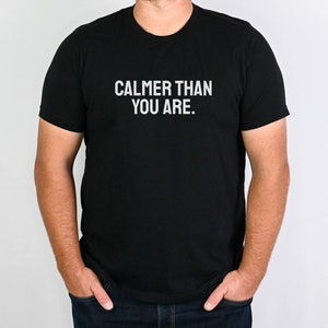 May include: A black t-shirt with the text "CALMER THAN YOU ARE." printed in white.