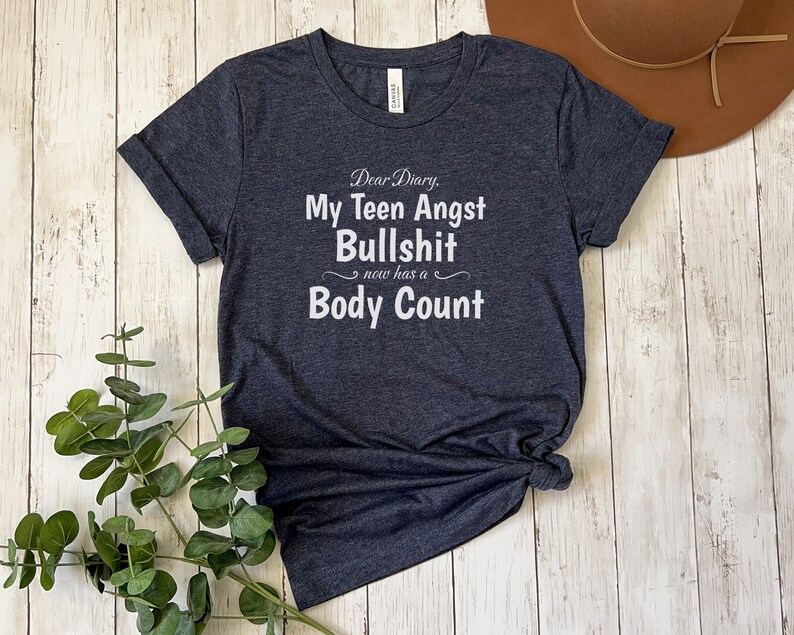 May include: A dark blue t-shirt with white text that reads "Dear Diary, My Teen Angst Bullshit now has a Body Count".
