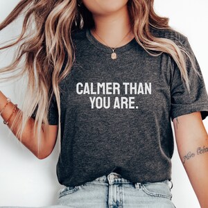 May include: A dark grey t-shirt with the text "CALMER THAN YOU ARE." printed in white.