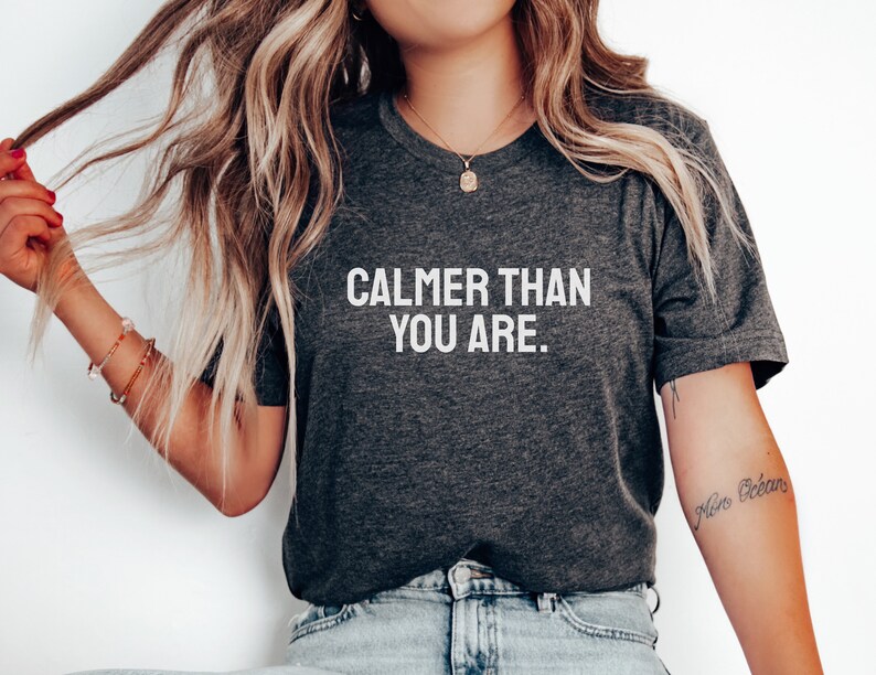 May include: A dark grey t-shirt with the text "CALMER THAN YOU ARE." printed in white.