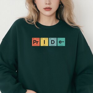 May include: A dark green sweatshirt with a graphic of the word "PRIDE" spelled out using the chemical element symbols for Promethium, Iodine, Deuterium, and Electron.