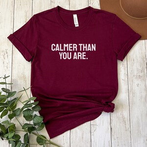 May include: Burgundy t-shirt with white text that reads "Calmer than you are."