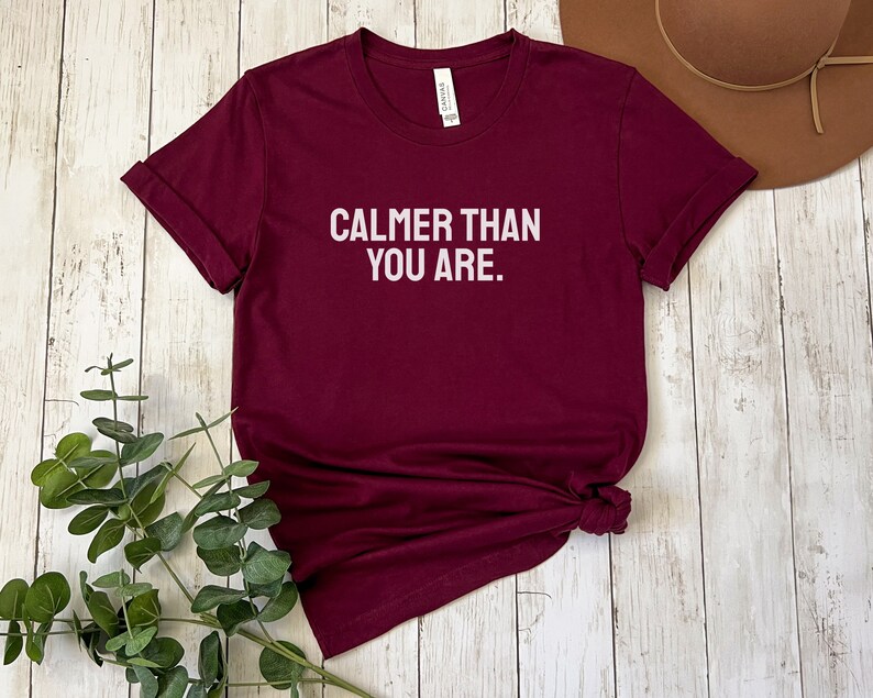 May include: Burgundy t-shirt with white text that reads "Calmer than you are."