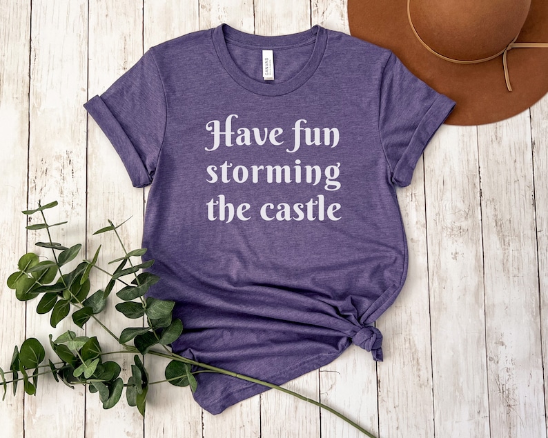 May include: Purple t-shirt with the text "Have fun storming the castle" in white.