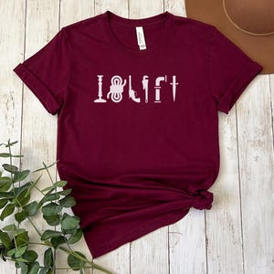 May include: Burgundy short-sleeved t-shirt with a white graphic of tools that spell out "I LOVE IT".