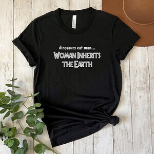 Peut inclure: T-shirt noir avec un texte blanc qui dit "dinosaurs eat man... WOMAN INHERITS THE EARTH"