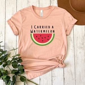 Może przedstawiać: R&oacute;żowy t-shirt z napisem "Niosłem arbuza" i grafiką plasterka arbuza.
