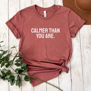May include: A maroon t-shirt with the text "Calmer than you are." printed in white.