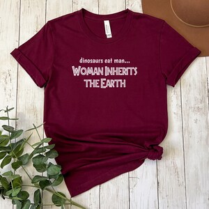 Peut inclure: T-shirt bordeaux avec un texte blanc qui dit "dinosaurs eat man... WOMAN INHERITS THE EARTH"